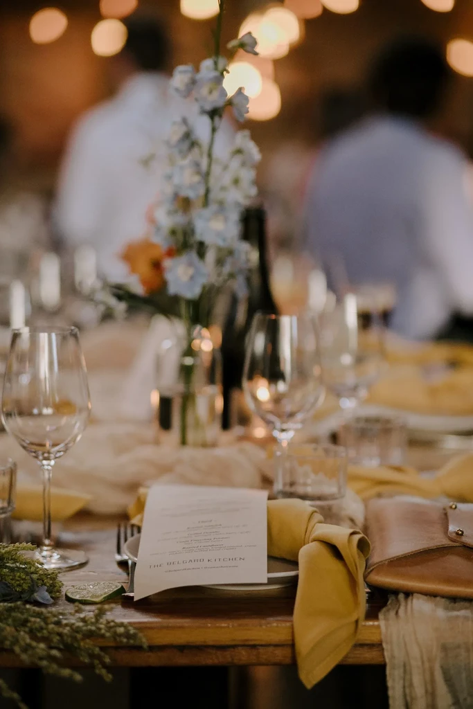 Dining table with 'The Belgard Kitchen' menu, floral centerpiece, bokeh lights.