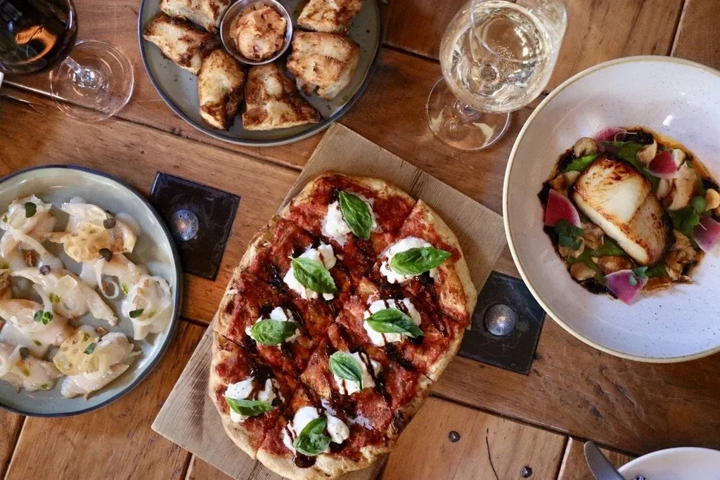 Rustic wooden table with pizza, fish, seafood, and wine.