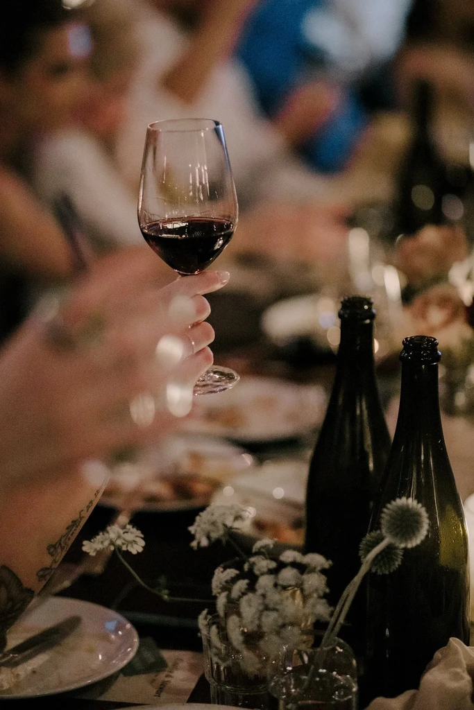 Close-up of hand holding a red wine glass at a warm dinner.