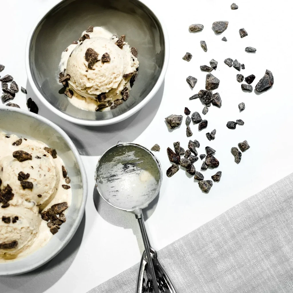 Two bowls of light ice cream with chocolate nibs and a scoop.