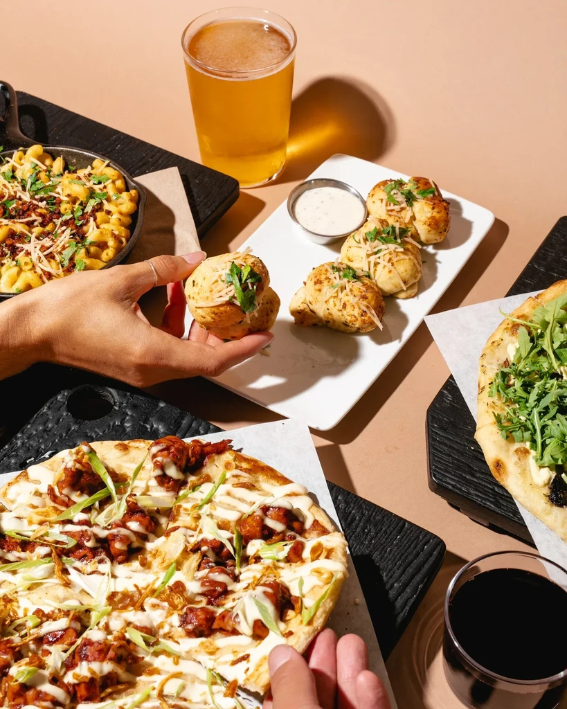 Overhead: Mac and cheese, garlic knots, two pizzas, drinks, and hands.