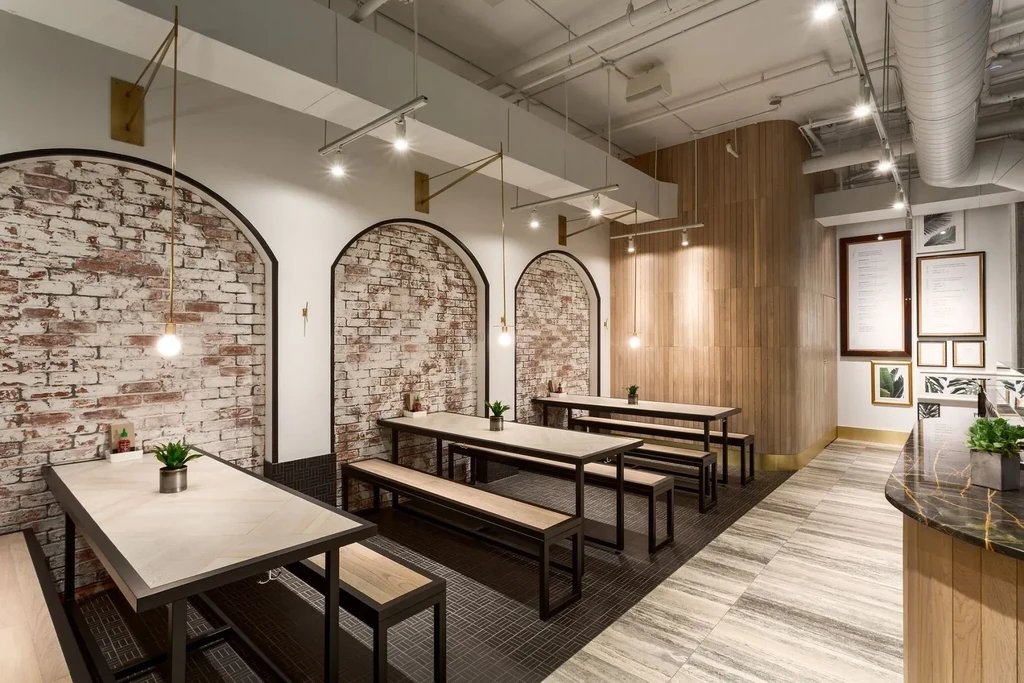 Contemporary restaurant with industrial ceiling, long tables, and brick arches.