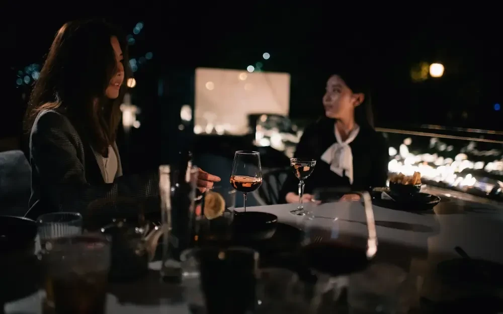 Two women conversing over drinks and snacks at a dim restaurant.