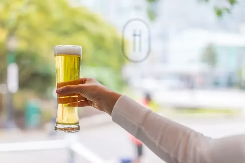 Hand holding golden beer with frothy head, blurred background.
