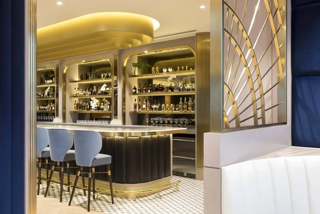 Dark bar counter with stocked shelves, golden light, and blue stools.