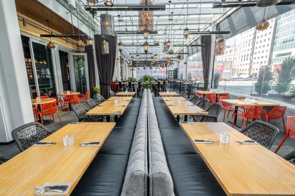Modern restaurant interior with central booth, varied seating, glass ceiling, city view.