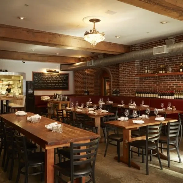 Rustic restaurant interior with brick walls, wooden tables, red booths, and chandelier.