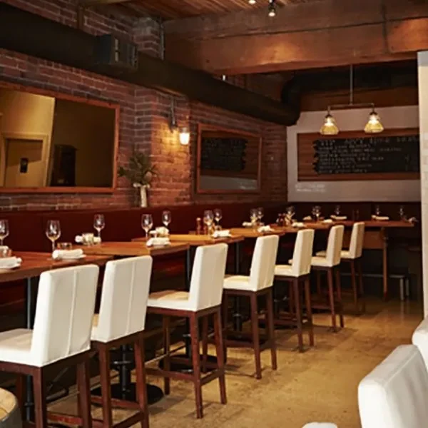Empty rustic-industrial restaurant with brick walls, banquette seating, and high-top tables.