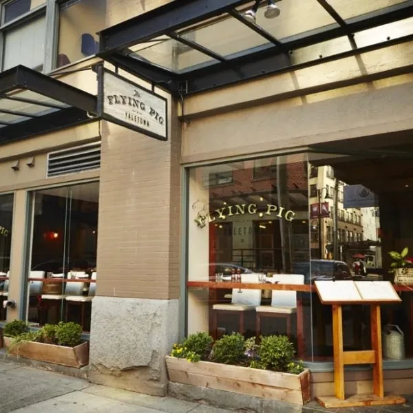 The Flying Pig restaurant exterior: large windows, brick columns, green planters.