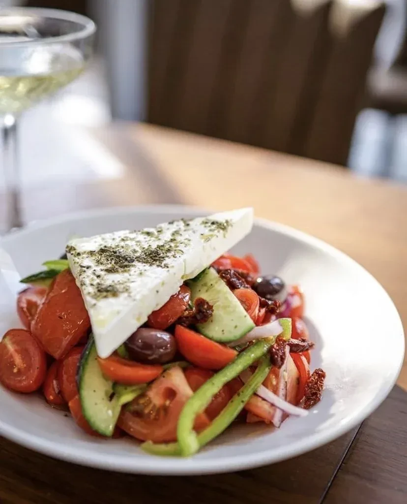 Greek salad with a large feta slice, tomatoes, cucumbers, and olives.