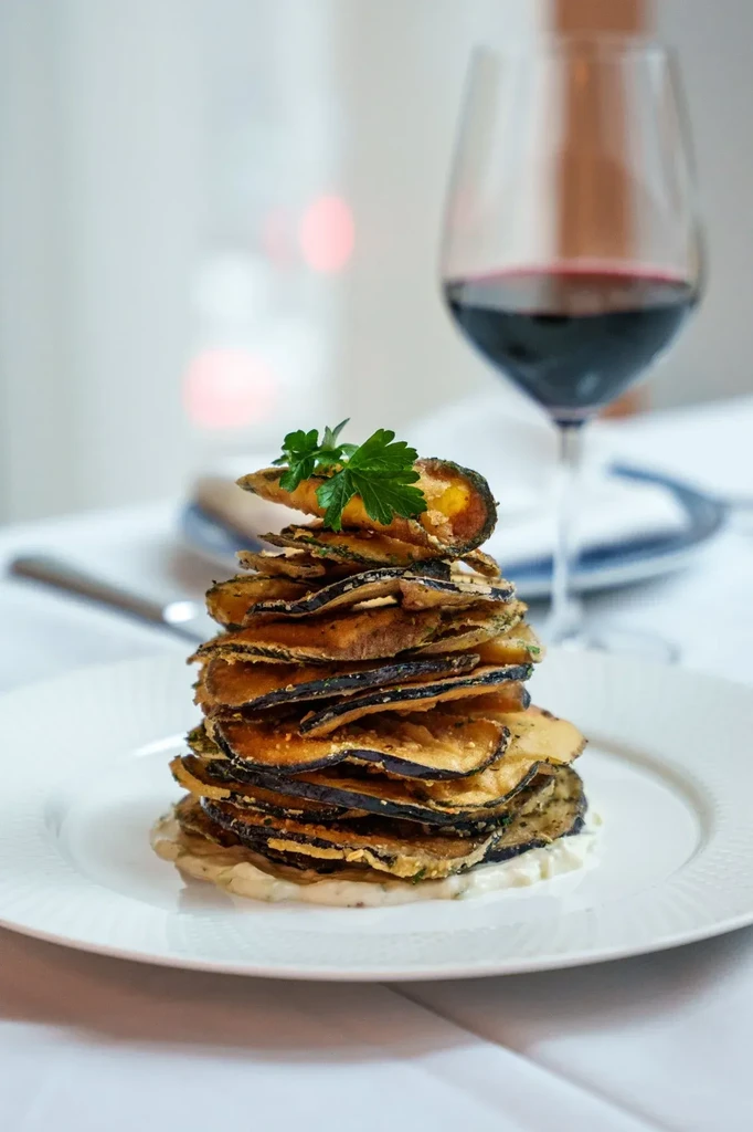 Stacked golden fried vegetable slices, creamy white sauce, and parsley garnish.