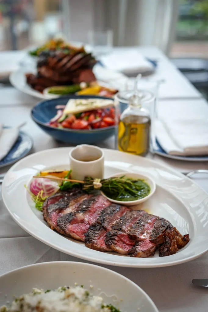 Medium-rare grilled steak on white plate with sauces and garnishes.