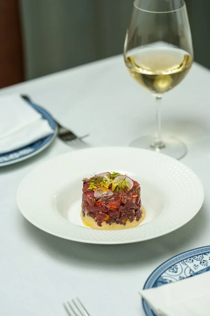 Cylindrical tartare dish with herbs, radish, wine, on a restaurant table.
