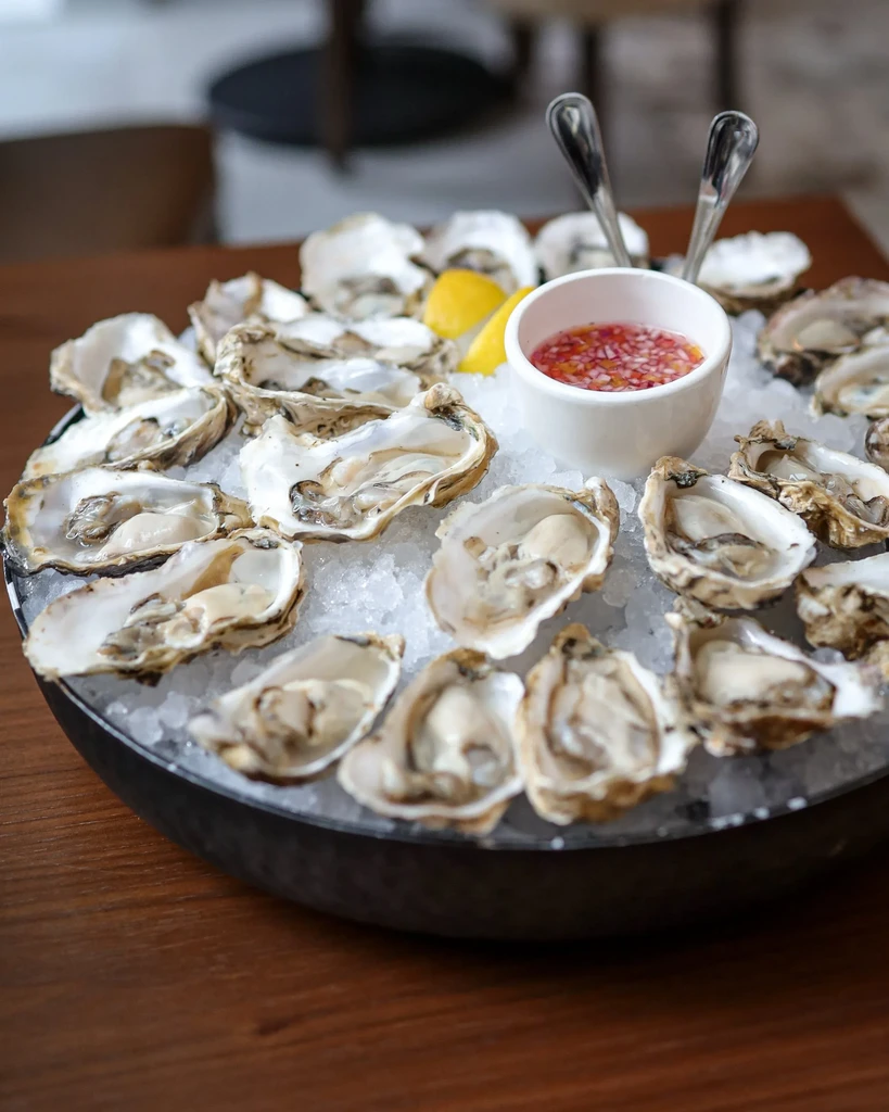 Fresh oysters on ice, with red sauce, lemon, and oyster forks.