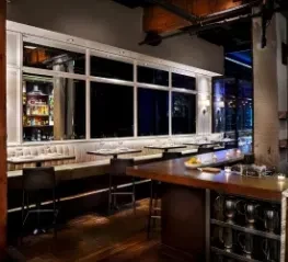 Interior view of a dimly lit restaurant bar with rustic-industrial decor.