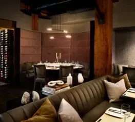 Upscale restaurant with warm lighting, tufted banquettes, round table, and wine rack.