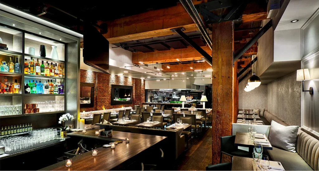 Modern upscale restaurant interior showing bar, dining tables, and open kitchen.