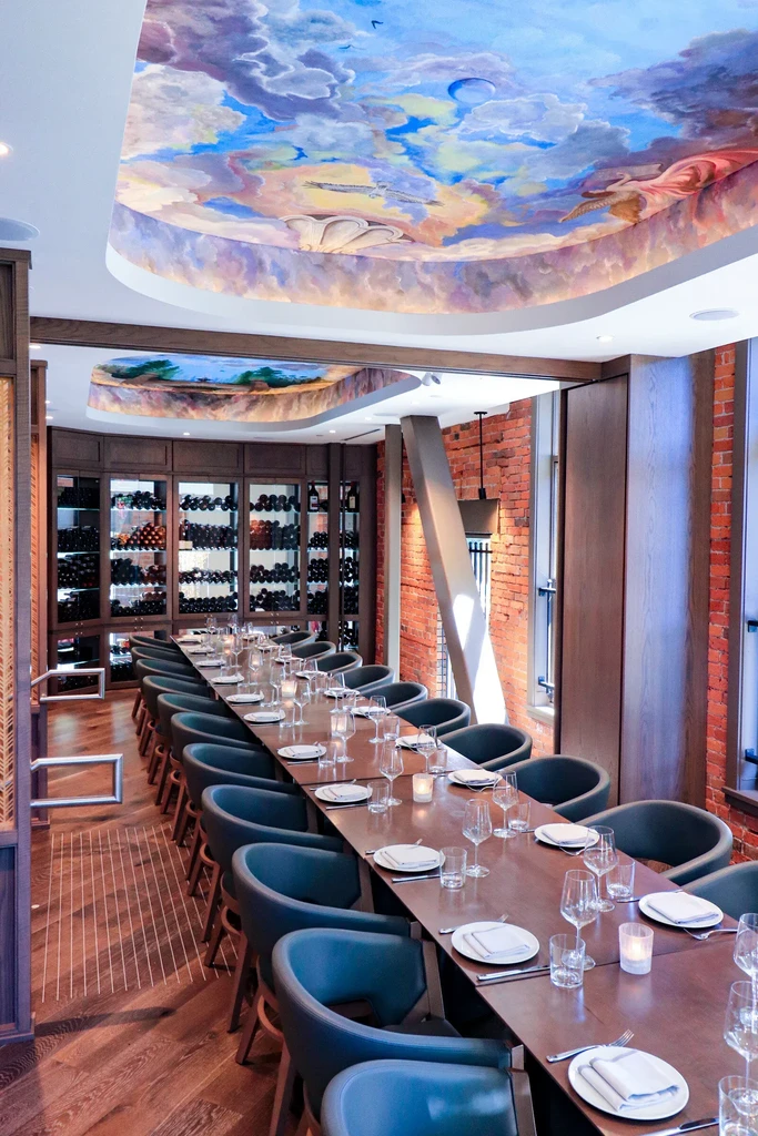 Private dining room with long set table, wine display, and ornate ceiling mural.