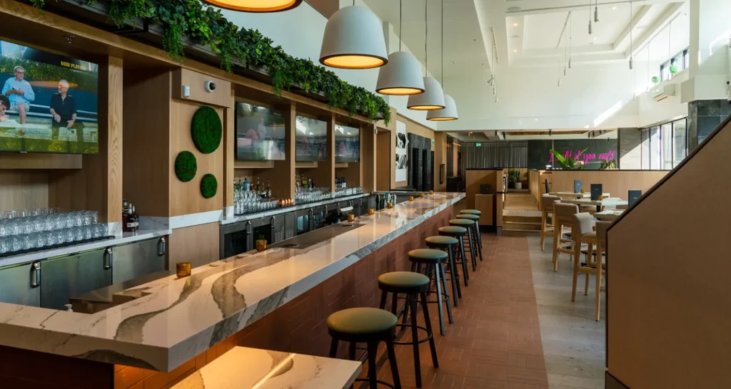 Modern bar with marble counter, green stools, and wood-paneled shelves.