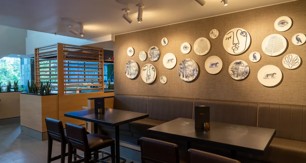 Empty modern restaurant interior: bench seating, ceramic wall plates, dark tables.