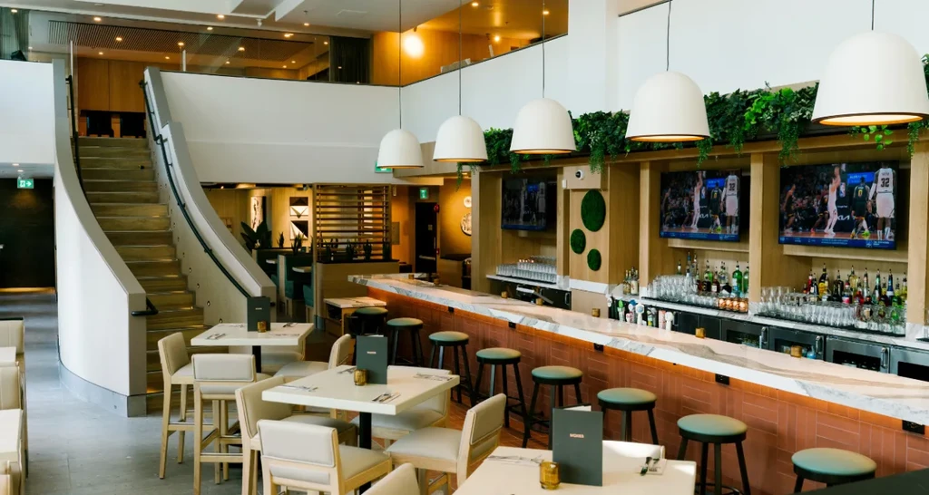 Modern restaurant interior with dining tables, stocked bar, and curved staircase.