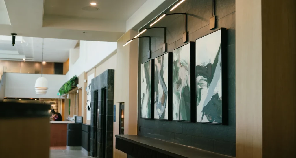 Dark textured wall with four abstract paintings and sleek accent lights.