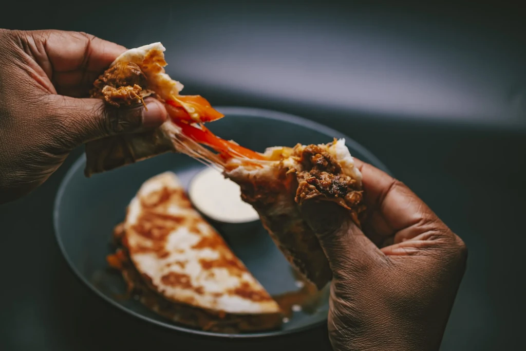 Hands pulling a cheesy quesadilla apart, revealing meat filling.