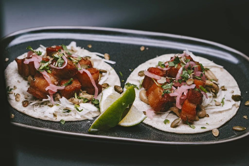 Two crispy pork belly tacos with cabbage, pickled onions, cilantro, lime.