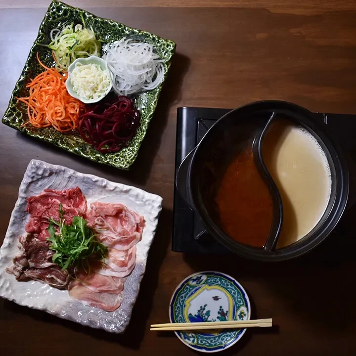 Fresh ingredients for hot pot: raw meat, colorful vegetables, and two broths.