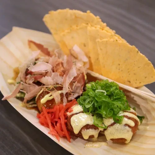 Takoyaki in wooden tray topped with sauce, scallions, ginger, bonito.