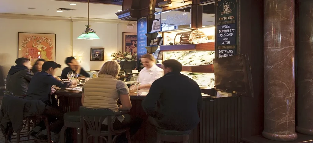 Upscale oyster bar interior with patrons, seafood display, and server.