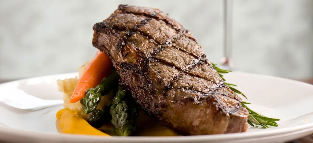 Grilled steak, carrots, asparagus, and yellow purée on a white plate.
