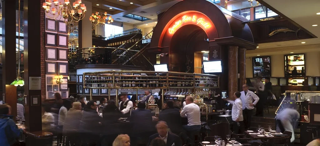 Lively, upscale restaurant interior with "Oyster Bar & Grill" neon sign.
