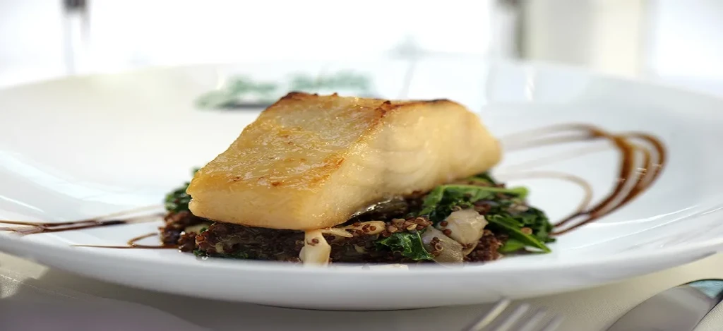 Close-up of pan-seared white fish on greens and grains with sauce.