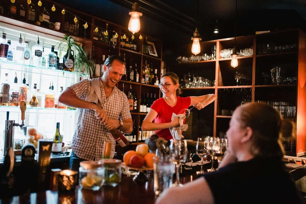 Smiling man and woman bartenders working behind a well-stocked bar.