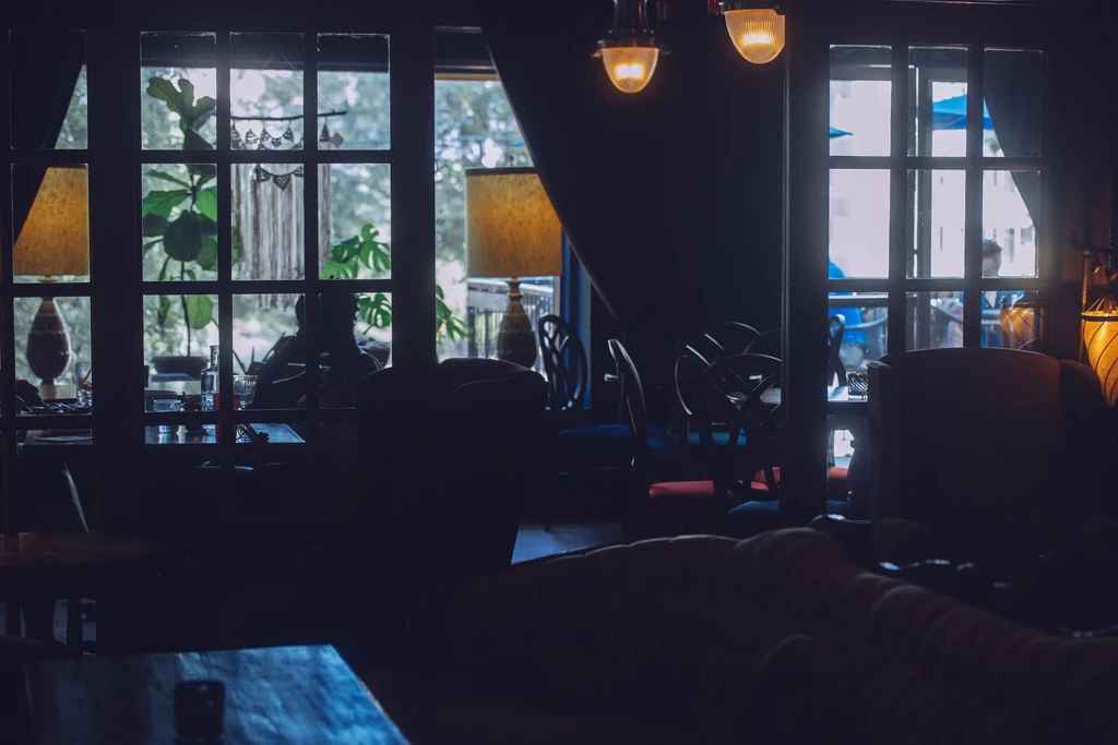 Moody, dark restaurant interior with large windows viewing a bright green patio.