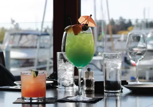 Colorful cocktails on a restaurant table overlooking a sunny marina.