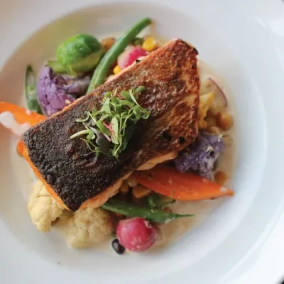 Pan-seared fish with crispy skin, microgreens, and colorful mixed vegetables.