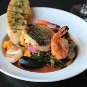 Plated gourmet seafood: seared fish, shrimp, scallop, mussels, vegetables, bread.