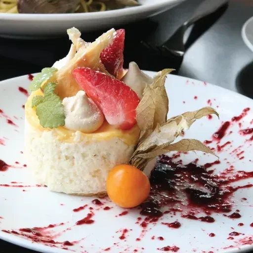 White and yellow layered dessert with strawberries, mint, physalis, berry coulis.