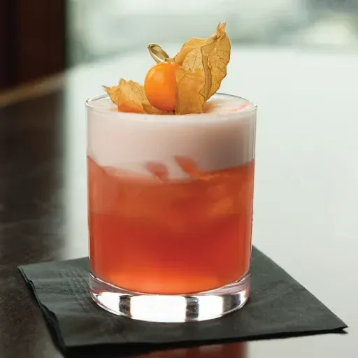 Two-layered cocktail with orange-red liquid, white foam, physalis garnish.