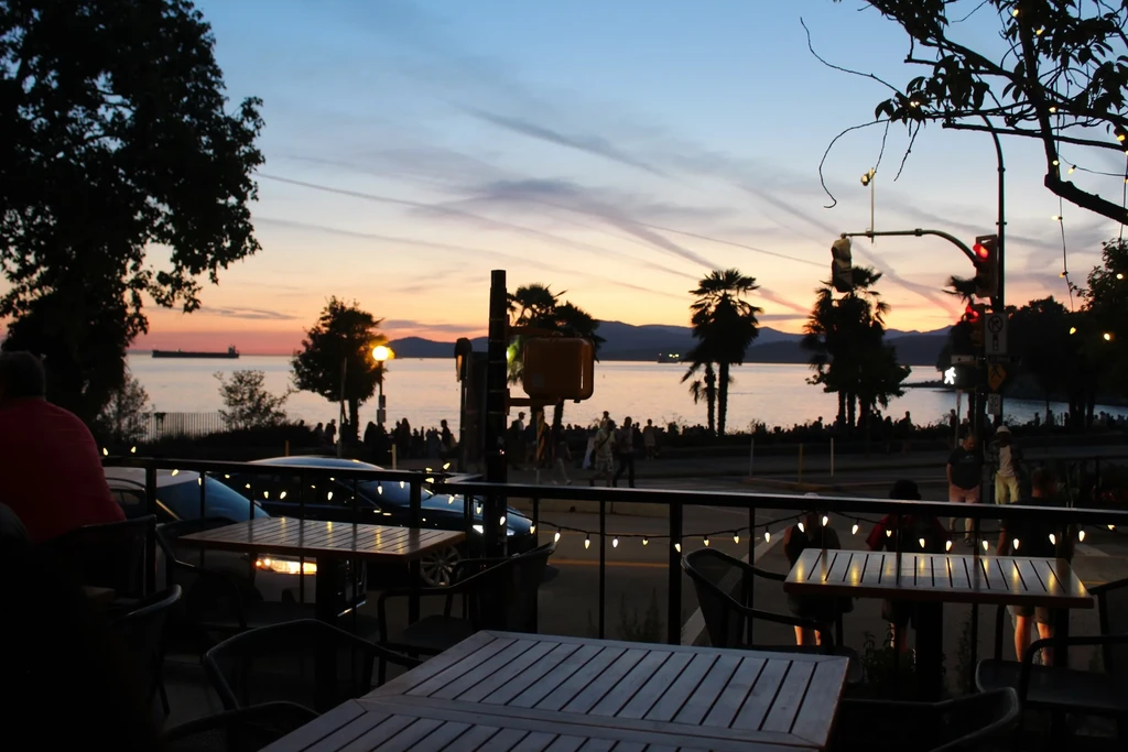 Dining patio overlooks a vibrant sunset over water with silhouetted figures.