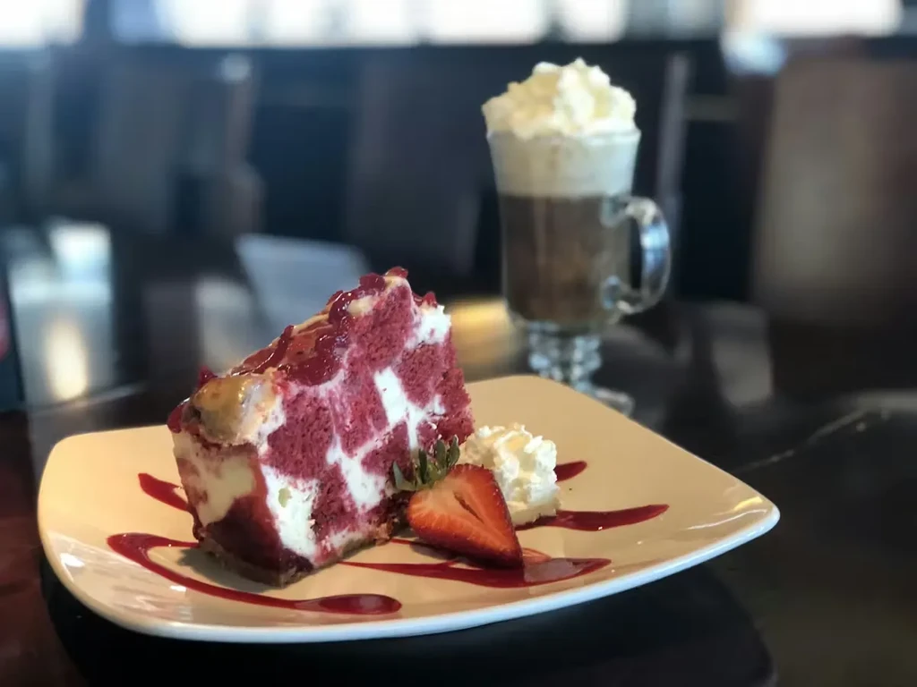 Checkered red velvet cheesecake slice with strawberry and crimson sauce.