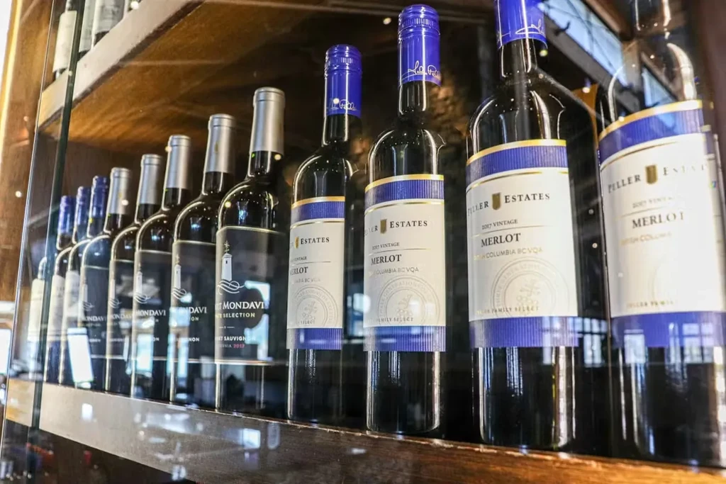 Red wine bottles from Peller Estates and Mondavi on a wooden shelf.