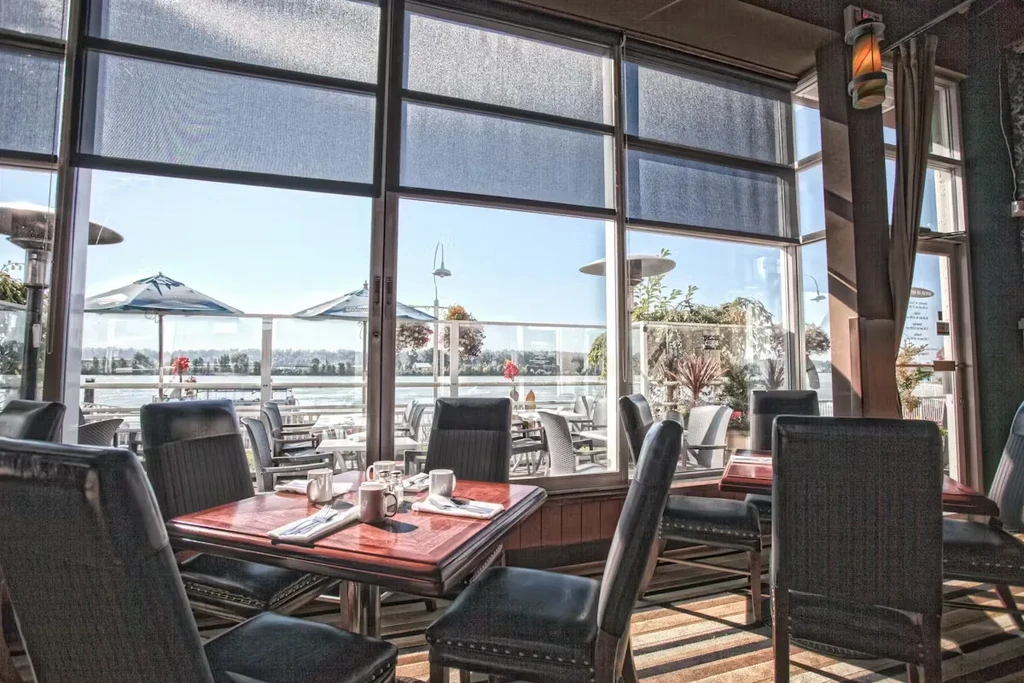 Empty, bright restaurant dining room with tables and a waterfront view.
