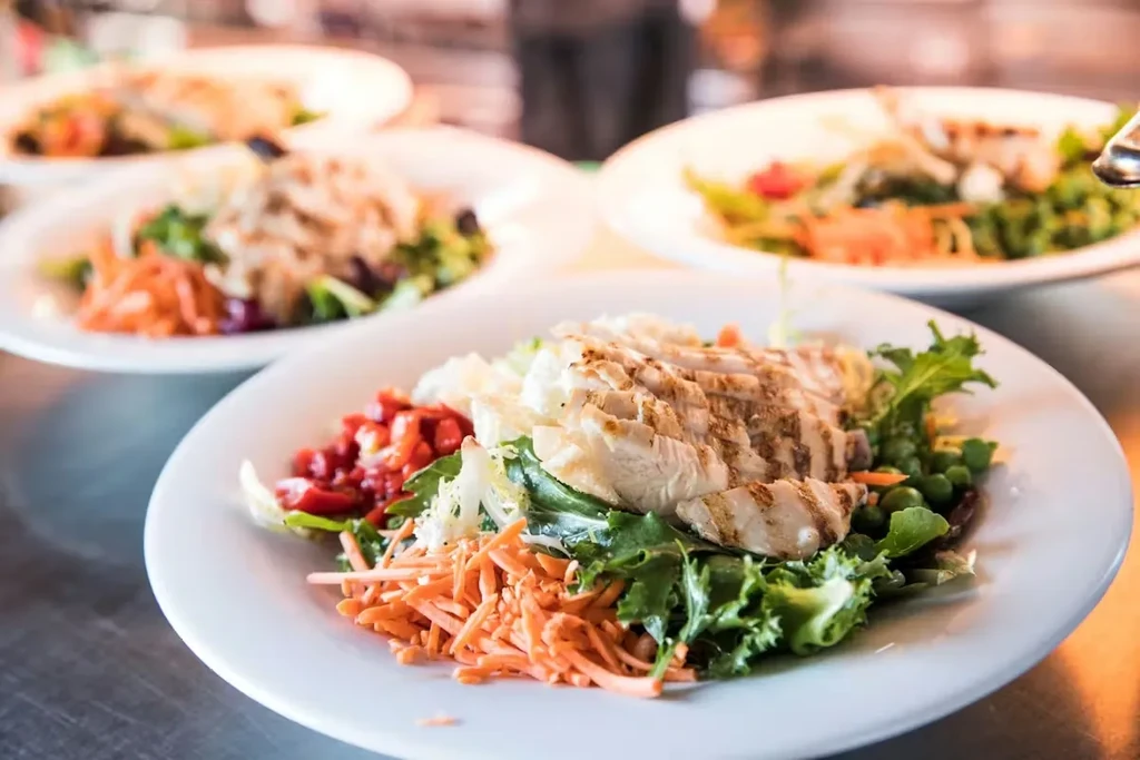 Fresh grilled chicken salad plate, other blurred plates in background.