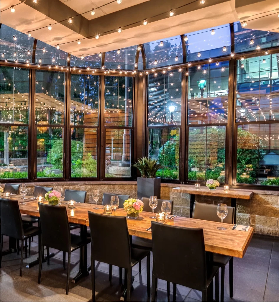Elegant restaurant with long table, string lights, and garden view.