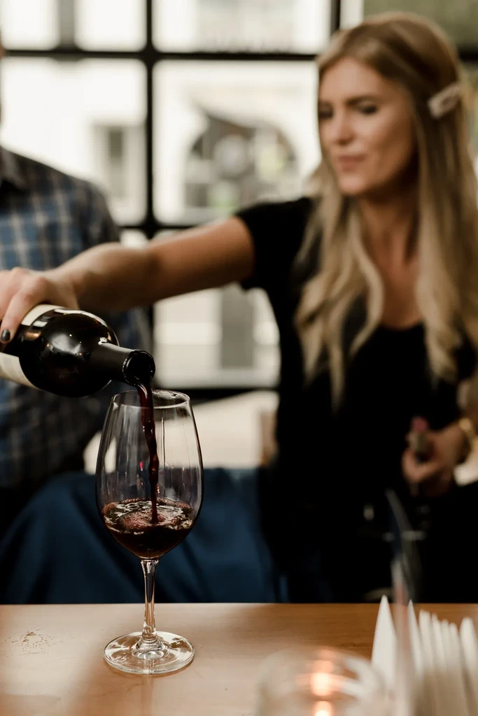 Close-up: Red wine pours from bottle into a clear glass.