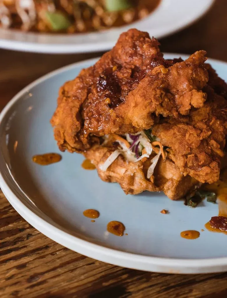 Fried chicken, waffle, and coleslaw with dark sauce on a blue plate.