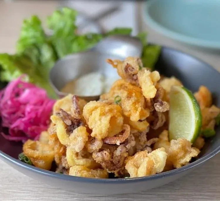 Close-up of golden-brown fried calamari with lime, sauce, and pickled vegetables.